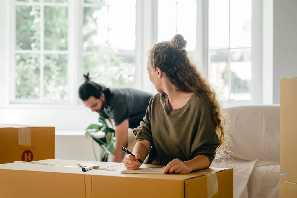 A woman is writing on a box while another woman looks on.